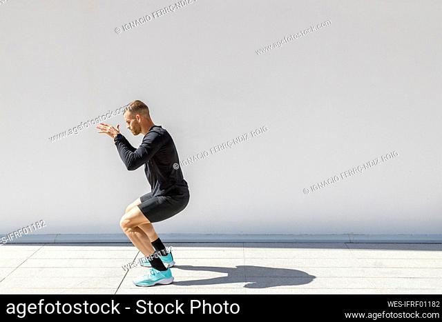 Young sportsman exercising while crouching on footpath