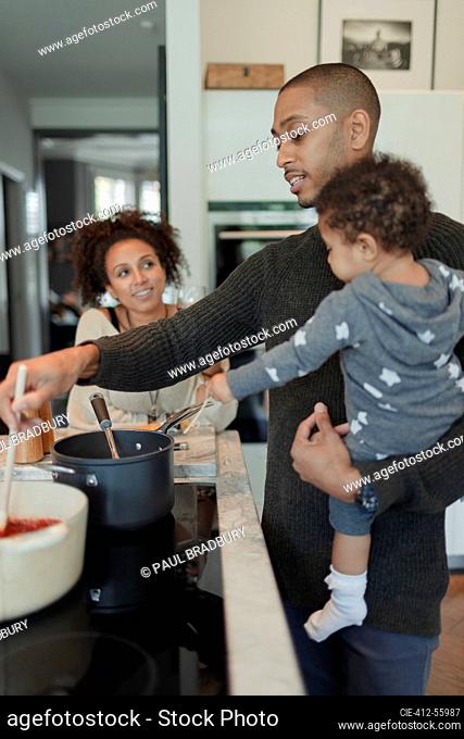 Couple with baby daughter cooking at kitchen stove