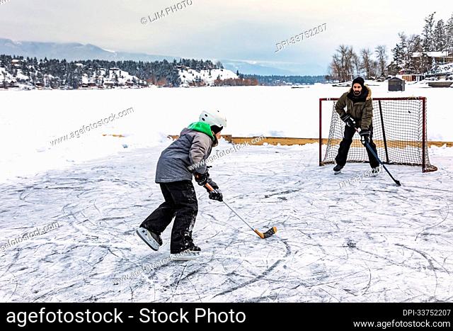 Father and his son playing hockey on a frozen Windermere Lake during the winter, Windermere Lake Provincial Park; Invermere, British Columbia, Canada