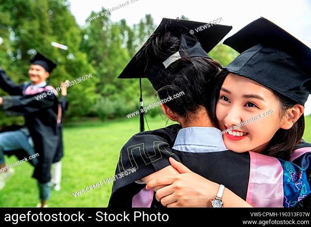Outdoor college students in bachelor of coats hug goodbye