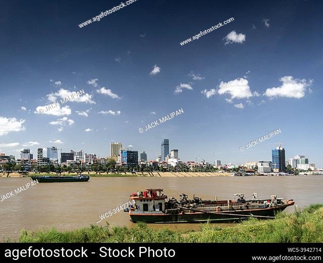 sand dredging boats on the Tonle Sap river with Phnom Penh city skyline in Cambodia