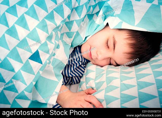 eight years old child sleeping in bed on pillow. Boy lying covered with blanket