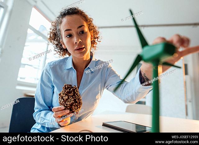Young engineer holding cookie examining wind turbine model at desk in office