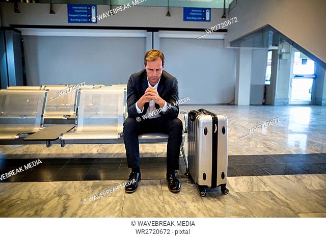 Tense businessman sitting in waiting area with luggage