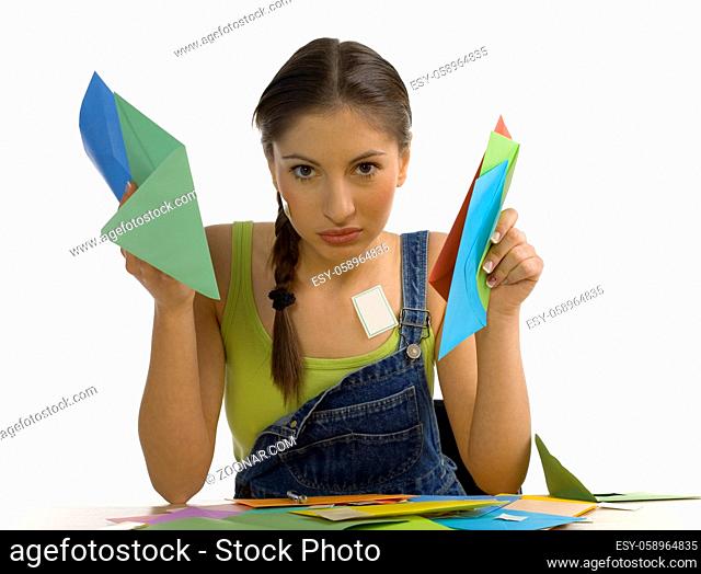 Young, beautiful and tired woman sitting at desk. Holding papers up and looking at camera. Front view, white background