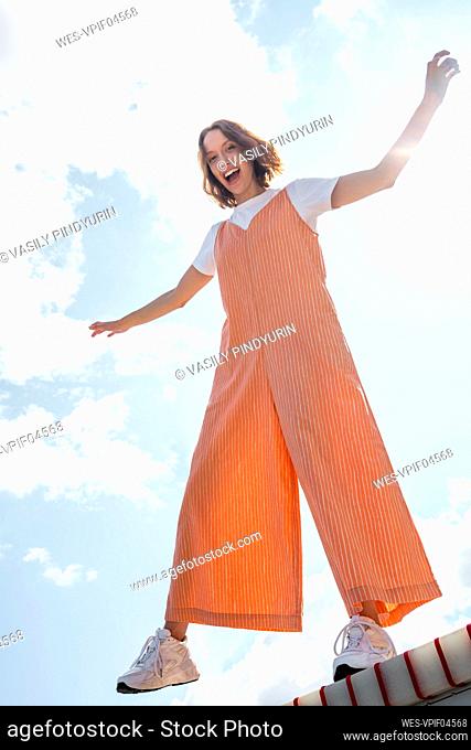 Carefree woman with arms outstretched standing on seesaw during sunny day