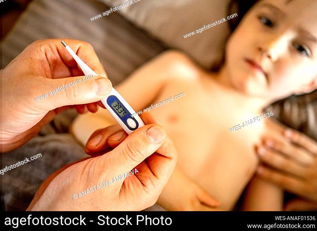 Father examining sick son with thermometer at home