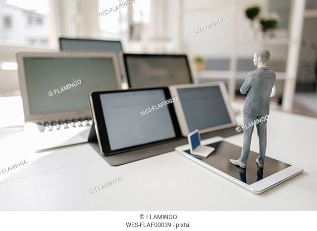 Businessman figurine standing on desk, facing mobile devices