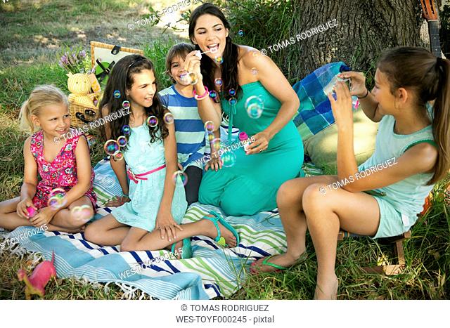 Happy mother with children blowing soap bubbles at tree