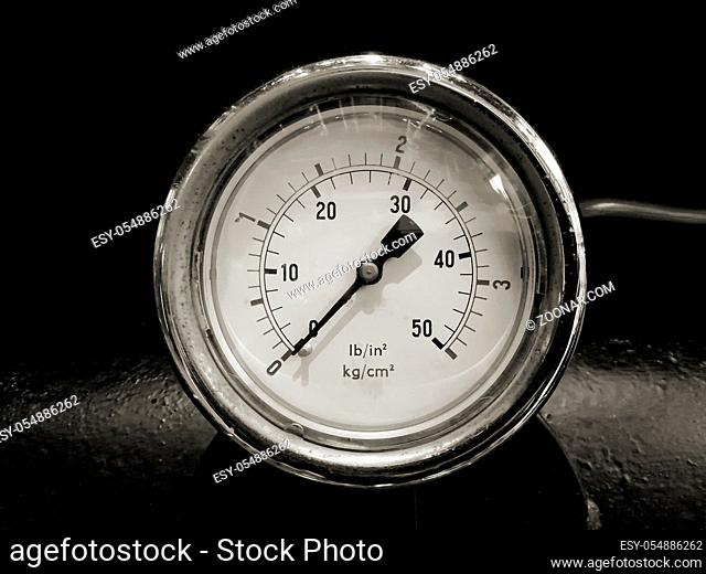 monochrome image of a round shiny pressurevintage gauge with numbers marked in psi and metric on the meter dial on industrial machinery