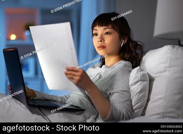 woman with laptop and papers in bed at night
