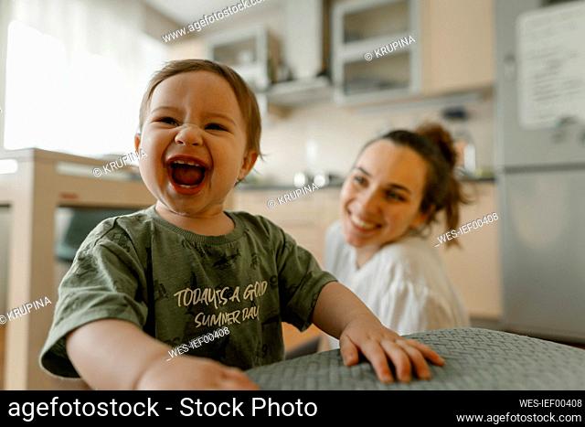 Cheerful baby girl laughing with mother in kitchen