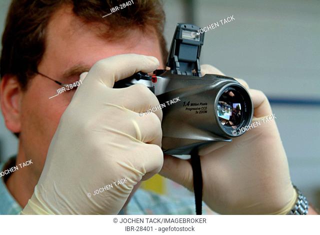 DEU, Germany, NRW: Forensic police investigator takes photos at a crime scene, with a digital camera