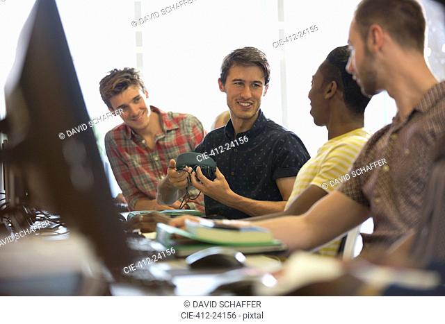 Group of smiling male students sitting at desks with computers and talking