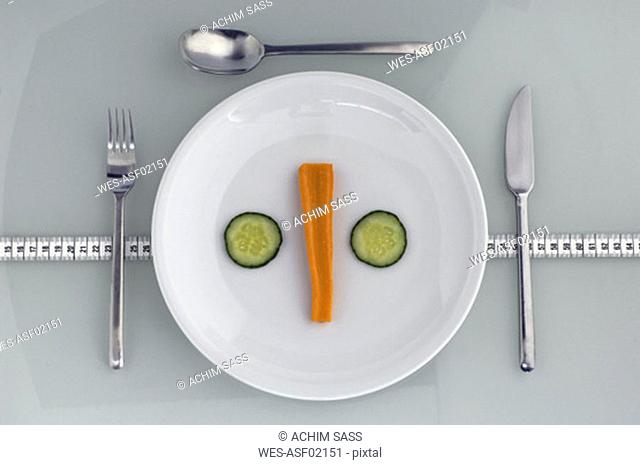 Plate with carrot and cucumber on measuring tape, close-up