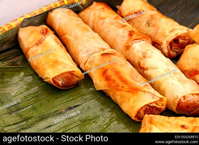 Portion of several deep fried crispy spring rolls, traditional Asian cuisine appetizer snack, served on green banana leaves, high angle view