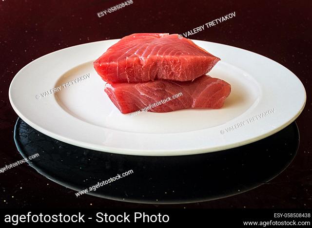 Fresh Tuna Steak on a white plate on a table as black background - fresh raw slices. Grain is the texture of the glass table