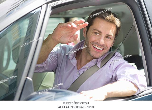 Man driving car, smiling out window and waving