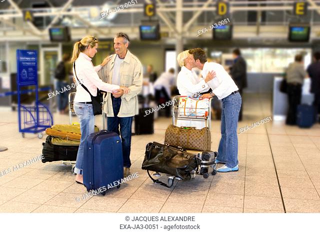 Senior couple hugging young couple with luggage at airport