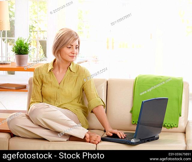 Attractive woman sitting on living room couch looking at laptop computer