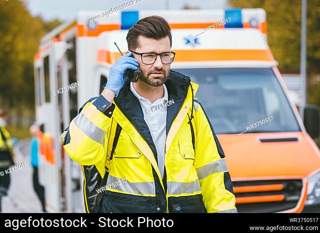Medic man talking to headquarter via radio in front of ambulance
