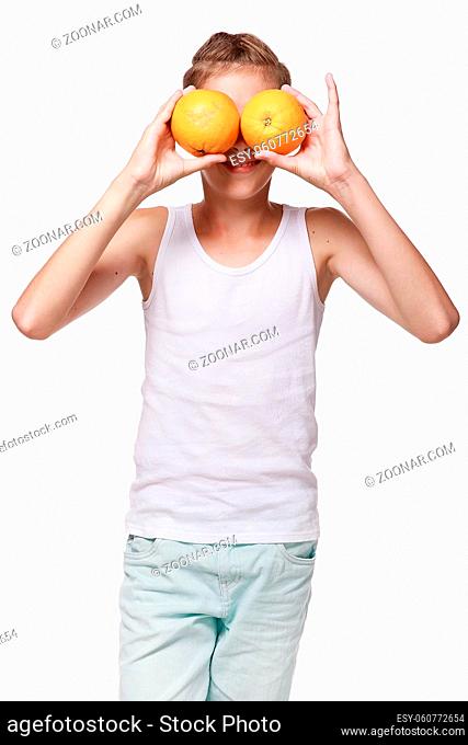 A young guy in a white shirt, closes his eyes with oranges, laughs, pampers, plays. On a white background in the studio. Emotions, fruit, lifestyle