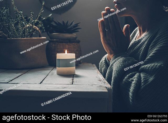 Concept of inner life balance and meditation with woman praying with clasped hands in front of a fire candle at home in the dark