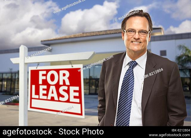 Handsome businessman in front of vacant office building and for lease real estate sign
