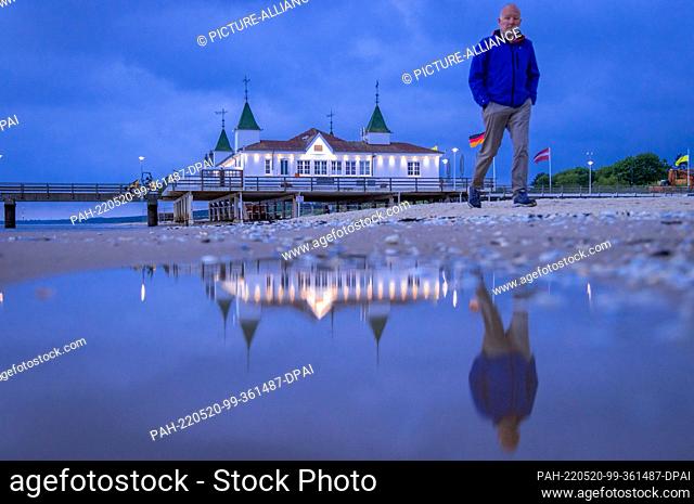 20 May 2022, Mecklenburg-Western Pomerania, Ahlbeck: A walker is on the Baltic Sea coast in front of the pier in the morning before sunrise