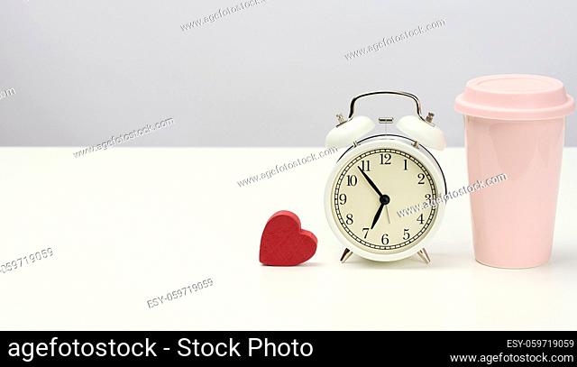 round retro alarm clock and pink ceramic cup with coffee on white table, copy space