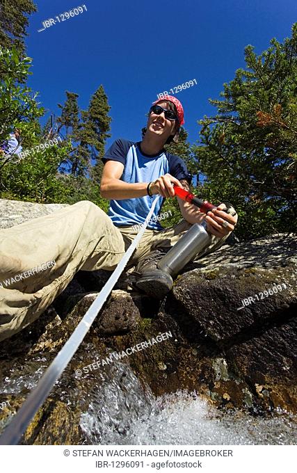 Young woman, hiker filtering fresh, potable water from a creek, Purification, protection from Giardia, historic Chilkoot Pass, Chilkoot Trail, Yukon Territory