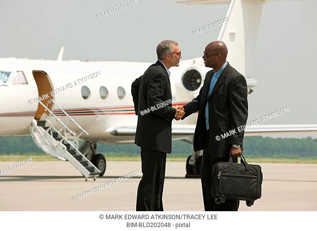 Businessmen shaking hands on airport tarmac