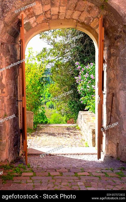 Castles Old stone arched entryway leads into landscape garden with green trees and flowers