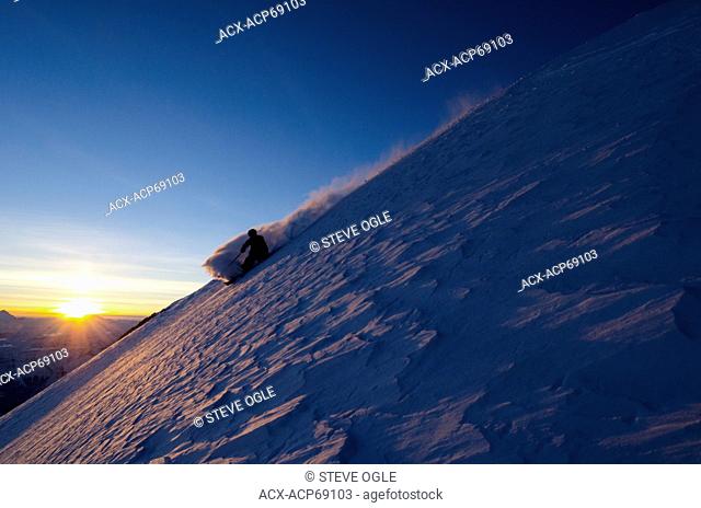 A skier descends a backlit slope above 11, 000' on Christian Peak in the Lyell Range, British Columbia Rockies