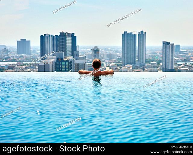Young man relax on the edge of the roof top swimming pool. Summer vacation concept