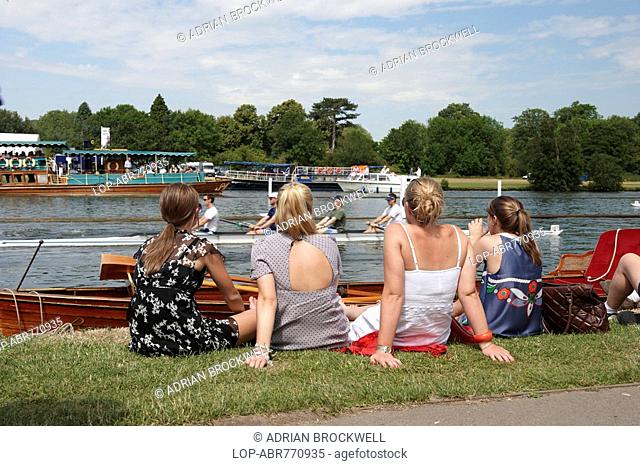 England, Oxfordshire, Henley-on-Thames, Four young women sitting on the riverbank enjoying the annual Henley Royal Regatta