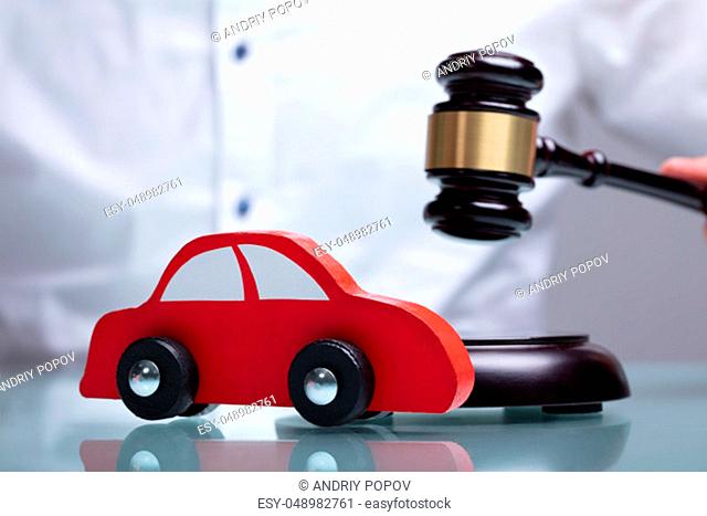 Close-up Of A Small Red Car In Front Of Judge Holding Mallet