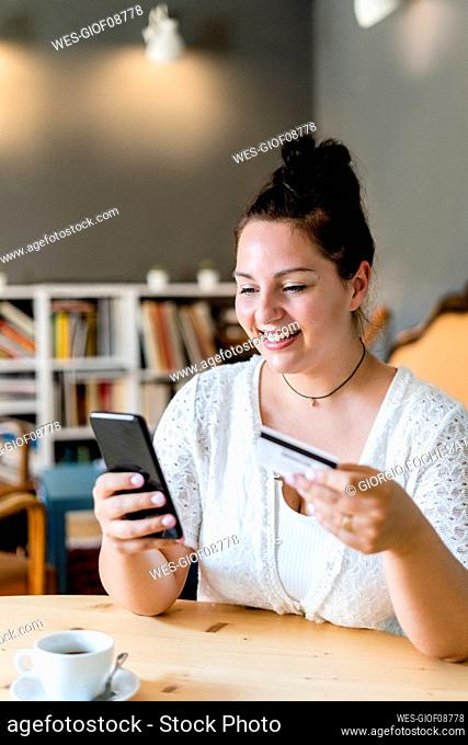 Smiling voluptuous woman doing online shopping over mobile phone in coffee shop