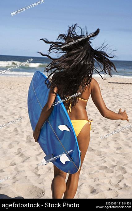 Mixed race woman running with surfboard on beach