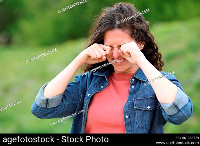 Stressed woman scratching itchy eyes standing in a green park