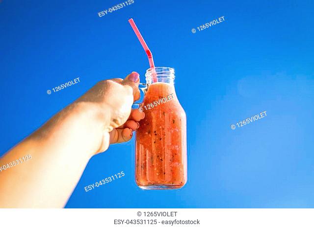 Woman holds a bottle of smoothie against the blue sky. Healthy breakfast. New day with beginning. Dieting