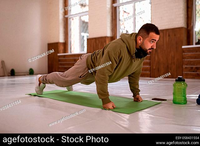 Muscular sportsman doing exercises alone in gym. Young handsome sports guy doing push ups exercise in empty gym with green bottle of water next to him all in...
