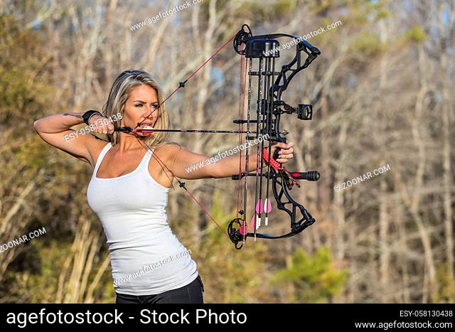 A beautiful blonde model posing with a bow and arrow outdoors