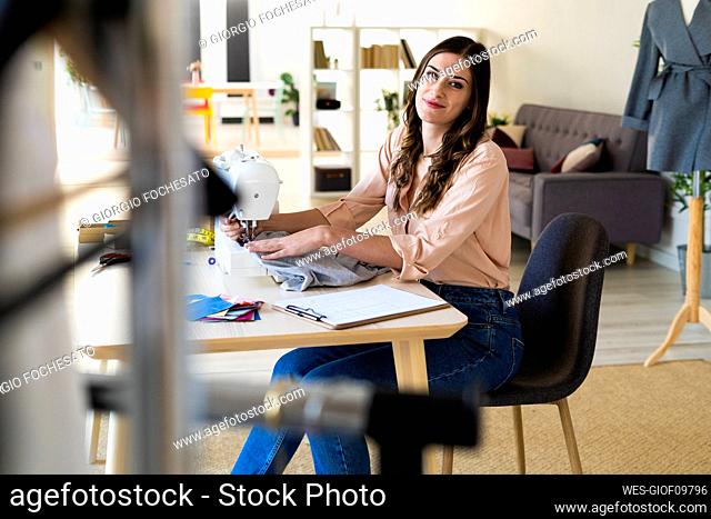 Smiling female designer sitting with sewing machine at studio