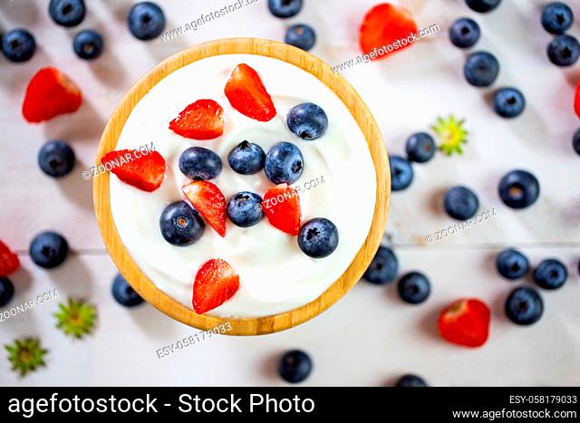 Wooden bowl full of yoghurt with strawberries and blueberries. Fresh berries with dairy cream in woody dish in focus. Little sweet healthy fruit blurred in...