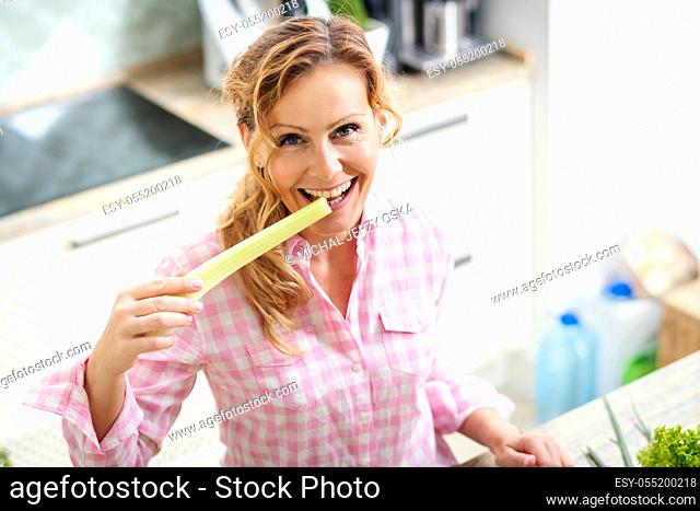 smiling woman holds and tastes fresh green celery in the kitchen