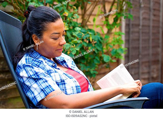 Mature woman on sun lounger reading book in garden
