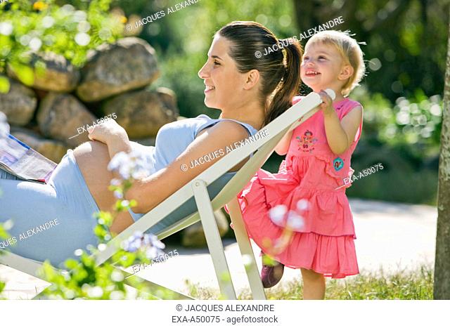 Young pregnant mother enjoying a summer day together with her daughter in the garden