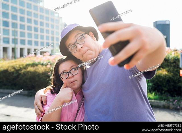 Teenage girl and boy making faces and taking selfie through mobile phone