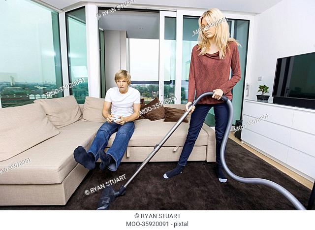 Woman vacuuming while man play video game in living room at home